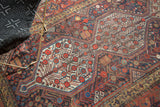 Vintage Qashqai rug's geometric medallion featuring pomegranate tree motifs in reds, indigo, and gold.