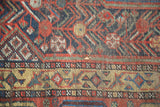 Qashqai rug detail: tribal red, indigo, gold patterns with foundation wear and small hole.