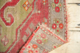 Storied antique Caucasian rug corner, revealing cochineal red, green motifs, foundation, and tattered fringe.
