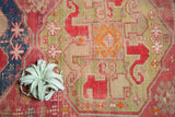Geometric animal figures and cloud band motif on an antique Caucasian runner, with cochineal red and green tones showing wear.