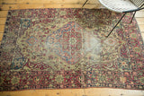 Antique Kermanshah rug corner detail with cochineal red floral border and antique ivory ground, showing wear.