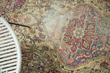 Antique Kermanshah rug detail: scalloped cochineal red medallion on ivory ground, soft blues, visible wear.