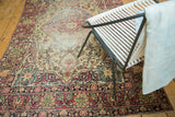 Antique Kermanshah rug's intricate cochineal red floral border and scalloped medallion contouring on ivory field.