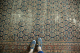 Person's feet on antique Malayer runner, highlighting repeating boteh pattern, intricate border, and wear.