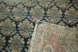 Antique Malayer rug runner folded, revealing intricate hand-knotted foundation, fringe, and boteh motif.
