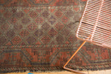 Wide meandering vine border and geometric lattice field on vintage Belouch rug in red, charcoal.
