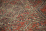 Textured pile of vintage Belouch rug, madder root red lattice, charcoal, visible wear.