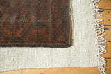 Corner of vintage Belouch rug, with madder root red meandering vine border and tattered fringe.