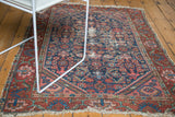 Worn North West Persian rug showing Herati motif, navy, rust tones, and frayed fringe.
