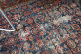 Visible foundation and wear on the navy and brick red vintage Herati motif rug.