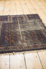 Antique Persian Belouch prayer rug showing indigo and brown patterns, tattered fringe, and visible foundation.