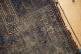 Worn corner of antique Belouch rug with exposed foundation, showing indigo and chocolate patterns.