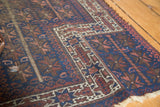Antique Belouch rug's geometric border, tribal indigo field, and visible side wear.