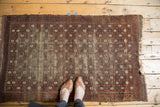 Antique Belouch rug with geometric charcoal, terra cotta, ivory pattern, showing wear, exposed foundation, and feet.