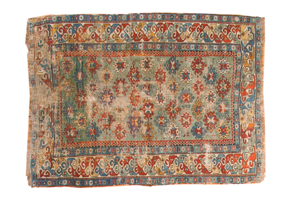 Antique Caucasian rug with a rare green field, featuring vibrant geometric motifs in red, blue, and gold.