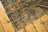 A collector's antique Caucasian rug showing its tattered corner and wear to the green field.