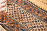 Vintage hand-knotted Belouch rug showing starbursts, pale rust borders, and time-softened charcoal details.