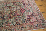Intricate mil fleur pattern, worn pile, and frayed edge of an Antique Kerman rug in blush and red.