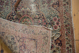 Antique Kerman rug's folded corner displays mil fleur pattern, visible foundation, and tattered side.
