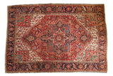 Vintage Heriz carpet with a rich red field, navy rectilinear medallion, and geometric floral patterns. 8'1