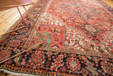 Rectilinear navy border with geometric floral motifs on a cherry red Heriz rug, showing pile wear.