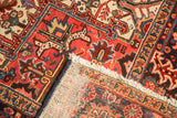 Vintage Heriz rug's folded corner, red geometric pattern, fringe, and exposed foundation.