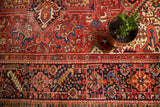 Rectilinear geometric floral motifs on a brick red Heriz field with navy blue border.