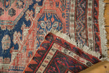 Folded vintage Soumac carpet corner, showing geometric patterns, navy, red, and macrame ends.