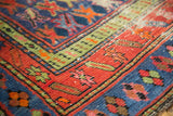 Geometric tribal patterns in brick red, sky blue, and green on a worn Caucasian rug.