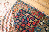 Vintage Caucasian rug corner with geometric plant motifs on indigo field, madder red borders.