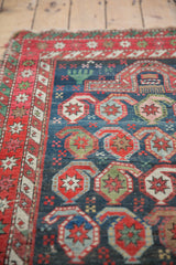 Antique Caucasian rug detail: red star burst border, indigo field with boteh, mehrab, and hands motifs.