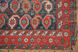 Antique Caucasian rug corner: red starburst border, green geometric outer border, tattered side.