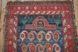 Antique Caucasian rug's indigo field with geometric mehrab, hands, and starburst red borders.