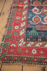 Antique Caucasian rug: red star burst border, sacred green motif, and tattered fringe.