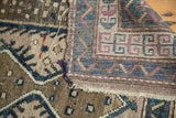 Vintage Caucasian rug fold showing geometric patterns, cobalt blue, mauve tones, and aged edge.