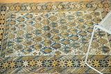 Geometric Caucasian rug border detail featuring abstract figural motifs and splayed floral elements.