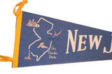 Close-up of vintage New Jersey felt flag, showing blue felt, yellow ties, and cream 'New J' text.
