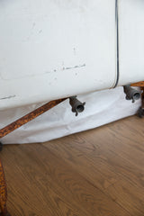 Detail of vintage galvanized wash tub, showing drain spouts, rusted frame, and distressed white finish.