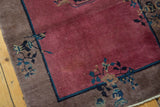 Art Deco rug corner with wine red field and camel border featuring blue plant motifs.