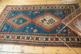 Vintage Caucasian rug lower left showing geometric border, indigo blue, and storied wear.