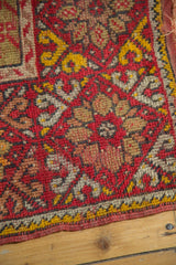 Vintage Mudjur prayer rug's worn corner, featuring cherry red field and saffron yellow floral border.