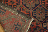 Folded antique Belouch rug shows hand-knotted trellis motif, rust and charcoal colors, and original selvage.