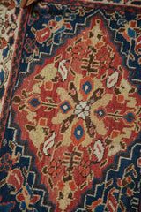 Expressive leaf and vinery motifs in brick red and indigo blue on an antique Persian rug.