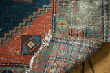 Antique Heriz rug edge revealing tattered fringe, visible hand-knotted foundation, and faded patterns.