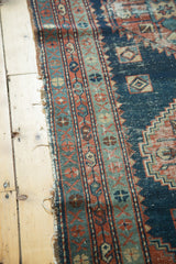 Antique Heriz rug side, showing faded brick red and teal geometric border with fraying edge.