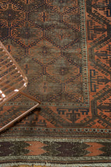 Detail of antique Persian Belouch rug showing rust lattice, scrolling border, visible foundation, and kilim.