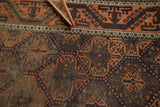 Terra cotta rust and dark aubergine geometric pattern detail on antique Belouch rug with visible wear.