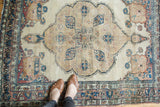 Antique Kerman rug border detail, showing visible wear and delicate floral vines in beige, blues, and reds.