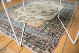 Antique Kerman rug corner, tattered edge, visible foundation, blue and cochineal floral patterns.