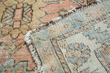 Close-up of vintage Lilihan rug's tattered edge, pale blush and green floral pile, and hand-knotted back.